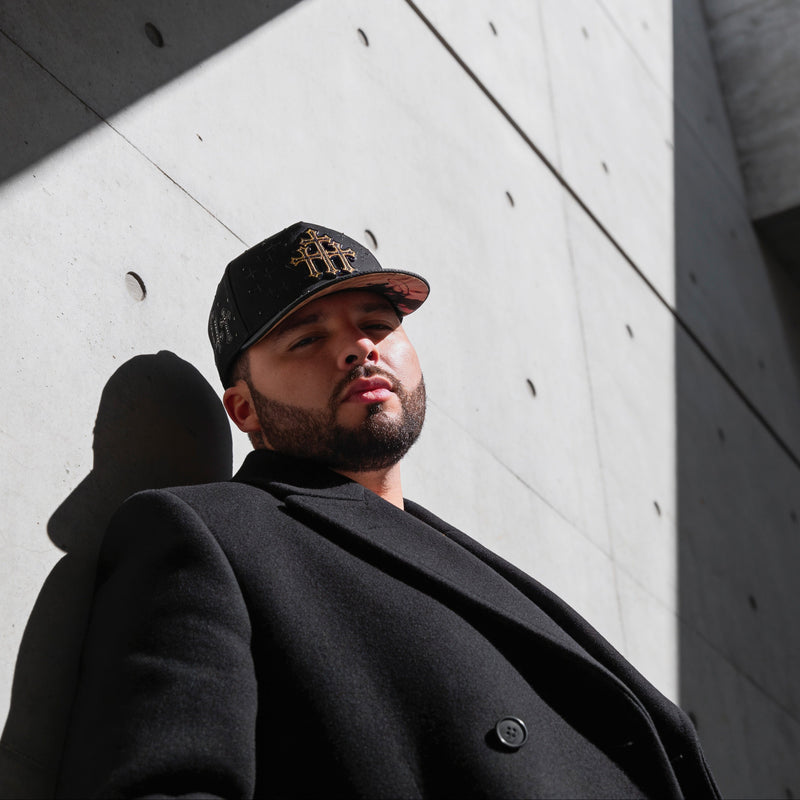 Man wearing a black cap and coat against a concrete wall with 'italiense' branding.